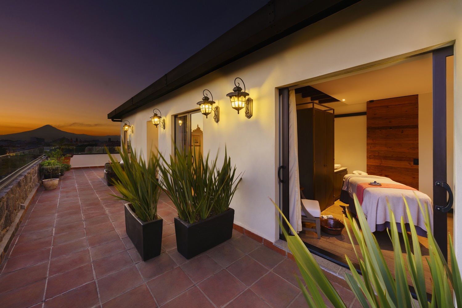 Terrace at sunset, lights illuminate spa room at Banyan Tree Puebla with mountain view.
